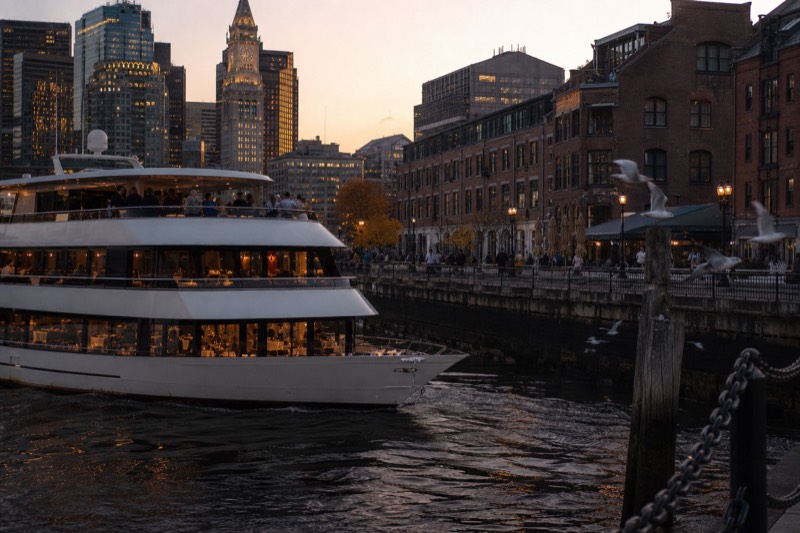 Odyssey dinner cruise yacht passing Rowes Wharf at dusk with plated dinner tables lit behind its windows