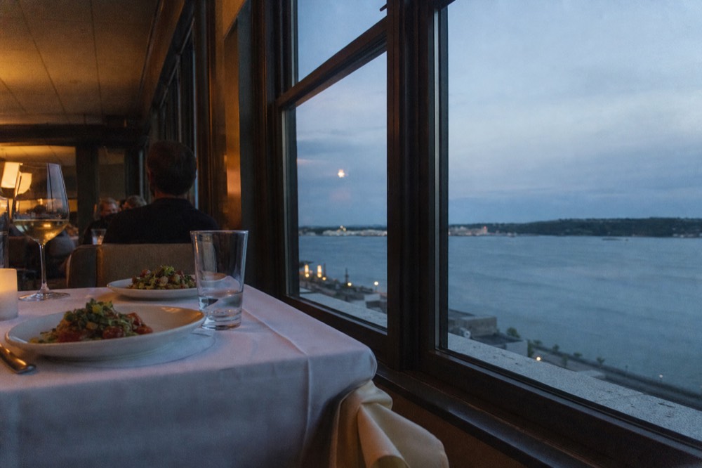 A plated dinner table set beside a window on a Boston Harbor cruise at twilight