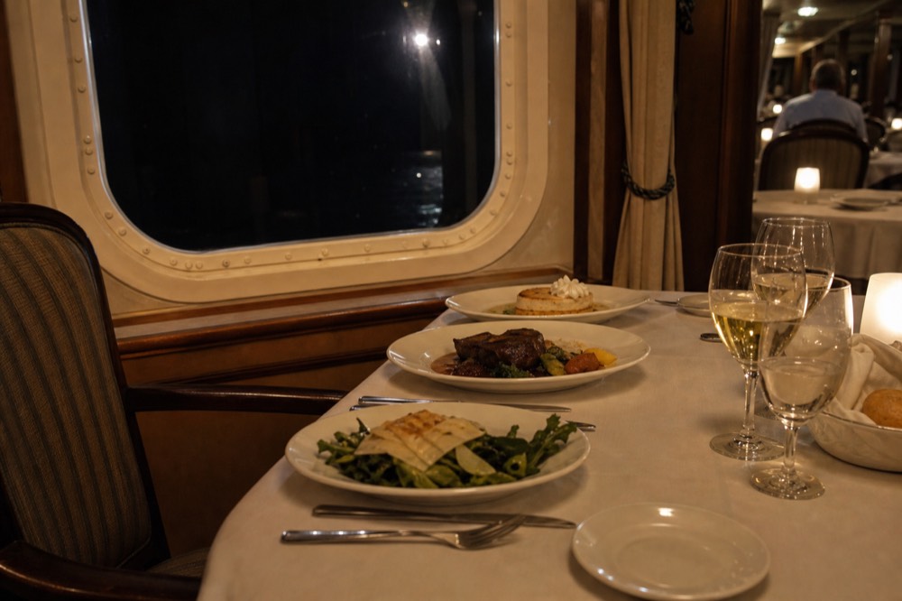 A set dinner table with plated courses inside a cruise ship dining room