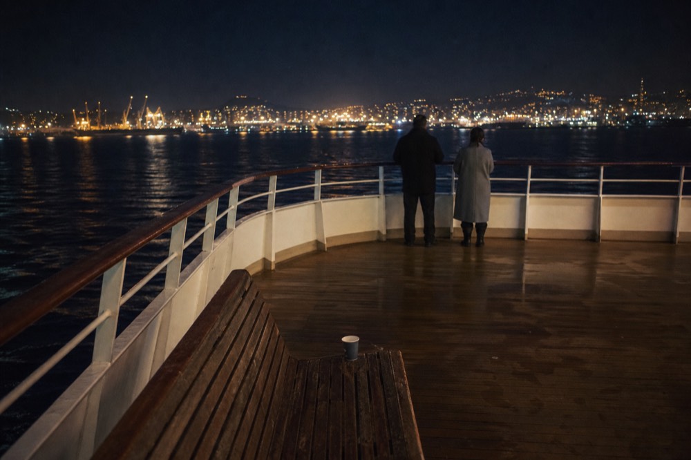 An outdoor observation deck of a dinner cruise vessel with Boston Harbor and city lights in the background
