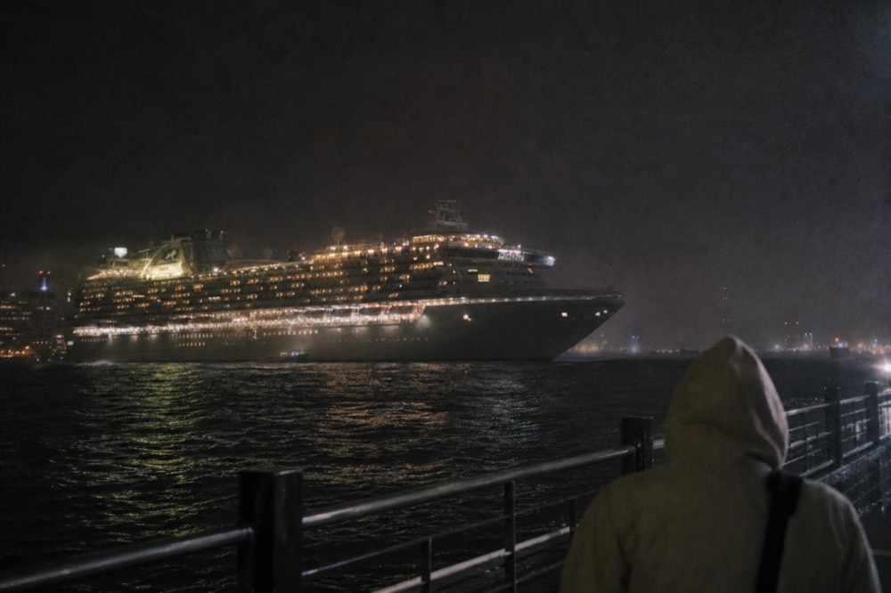 An illuminated cruise vessel underway on dark harbor water at night