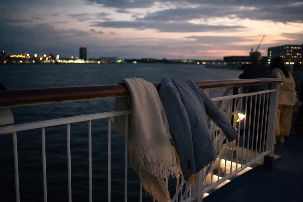 A woman's wrap and a man's sport coat draped over a railing on a dinner cruise deck at dusk