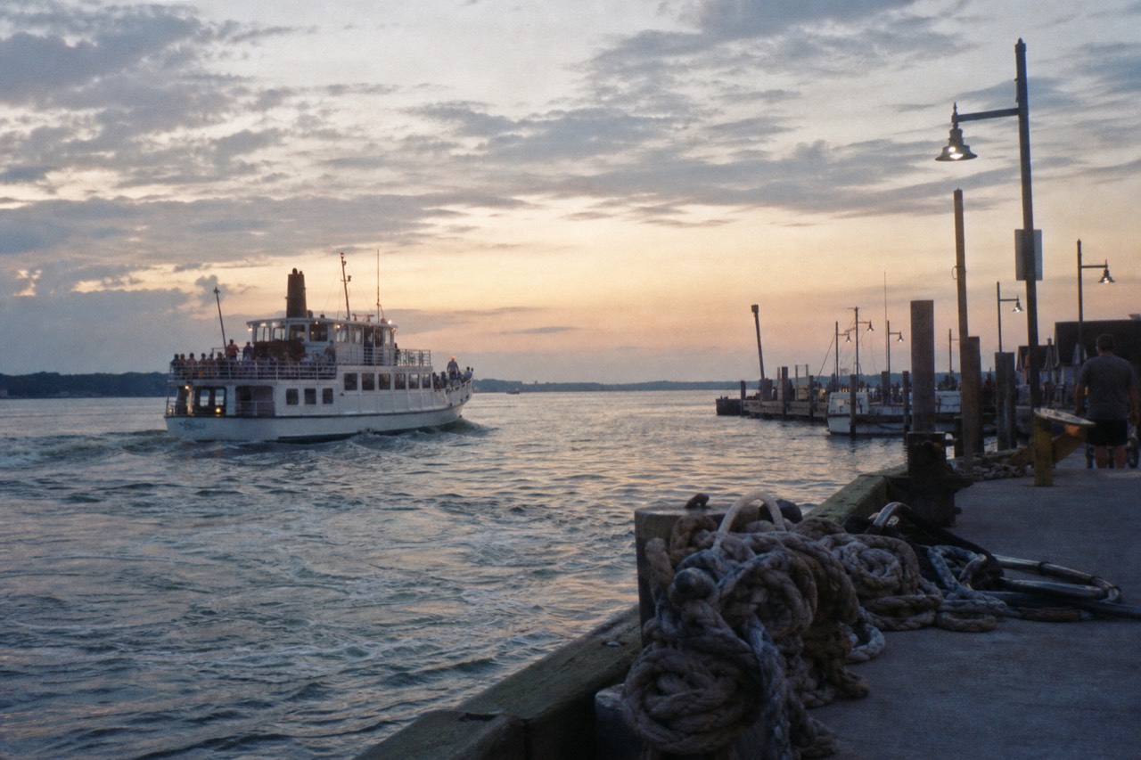 A dinner cruise vessel pulling away from a Boston pier at dusk