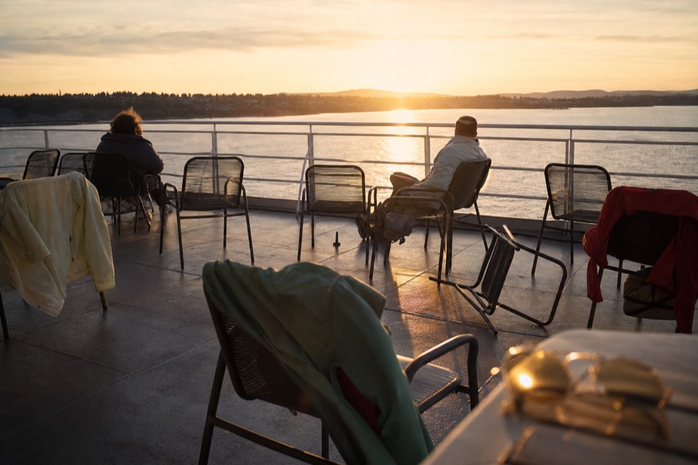 Passengers' jackets and wraps draped over deck chairs on a harbor cruise at sunset