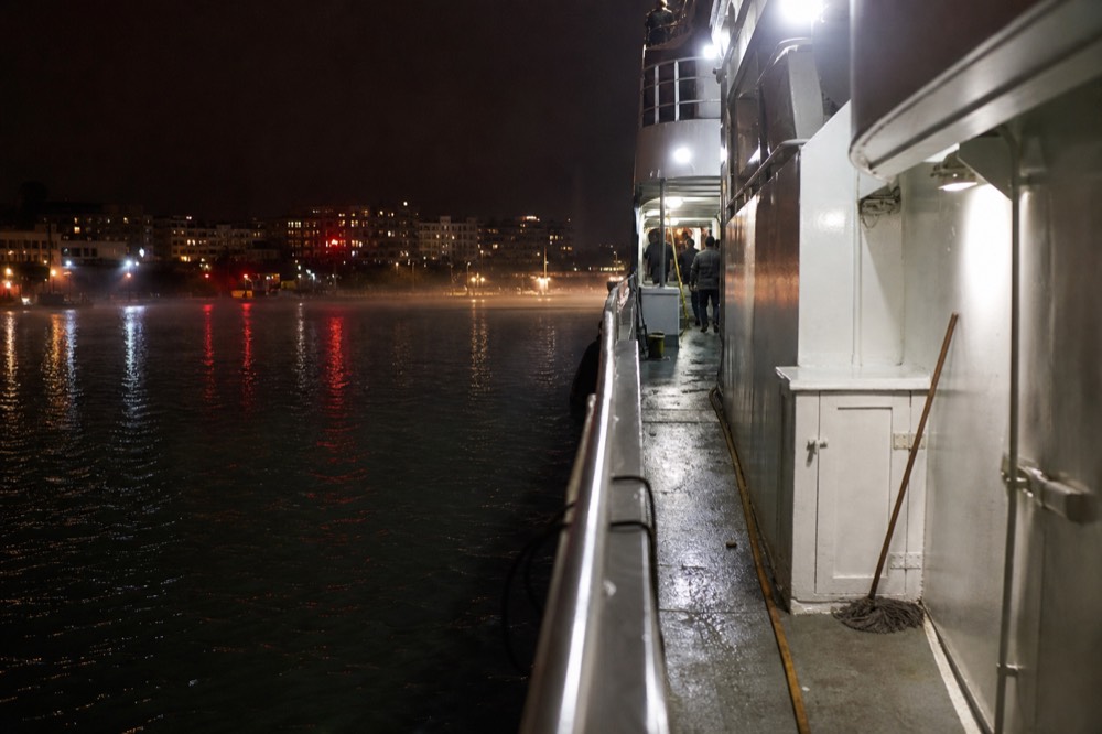 A dinner cruise vessel moored at a Boston pier at night with city lights reflecting on the harbor water