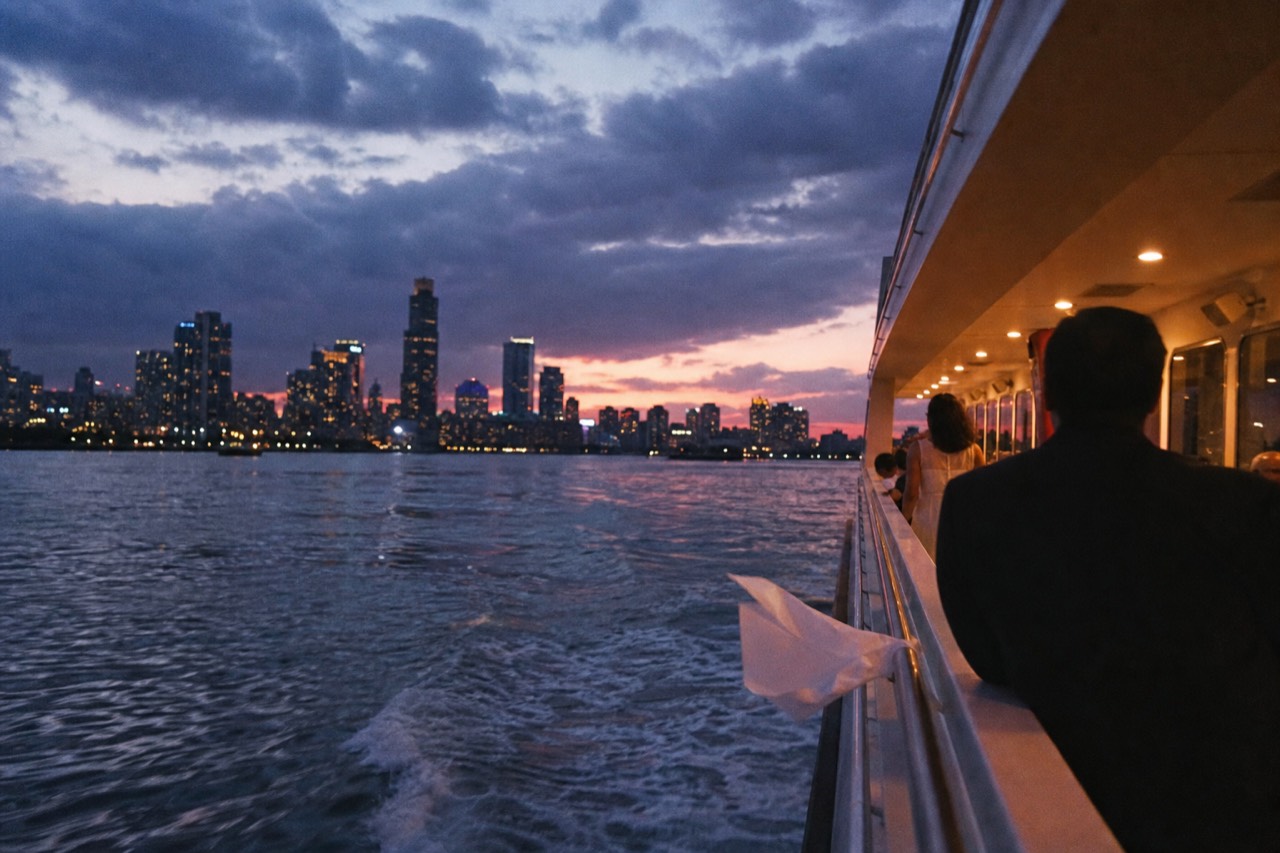 A dinner cruise vessel underway on Boston Harbor at dusk with the city skyline behind it