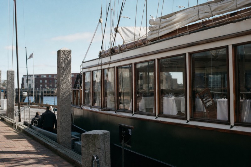 Sleek dining vessel with white-tablecloth tables moored at a brick wharf on Boston Harbor
