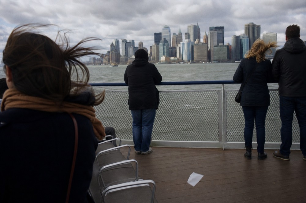 Passengers on an open-air cruise deck with Boston skyline