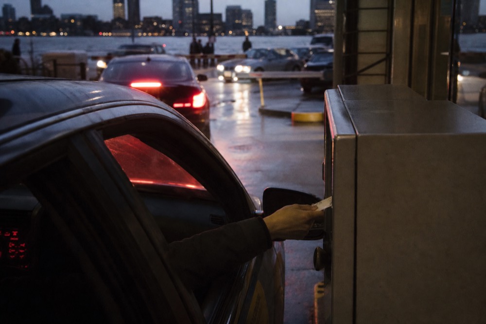 Cars lining up at a Boston waterfront parking garage pay station in the evening