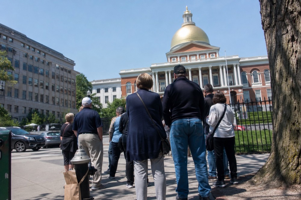 A guide gesturing toward the Massachusetts State House golden dome while a small group listens