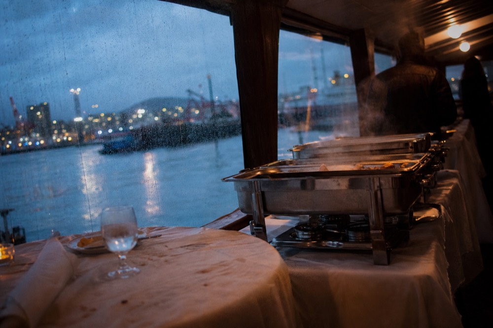 A buffet dinner spread on a cruise ship dining deck with harbor light through the windows