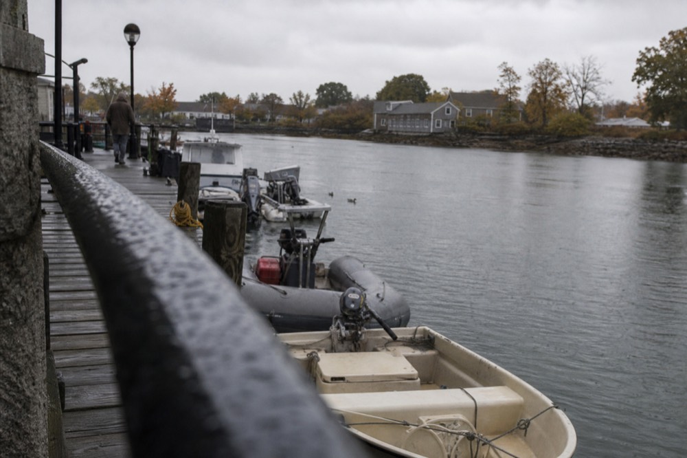 The Boston Harborwalk at water level with boats moored along a wooden pier