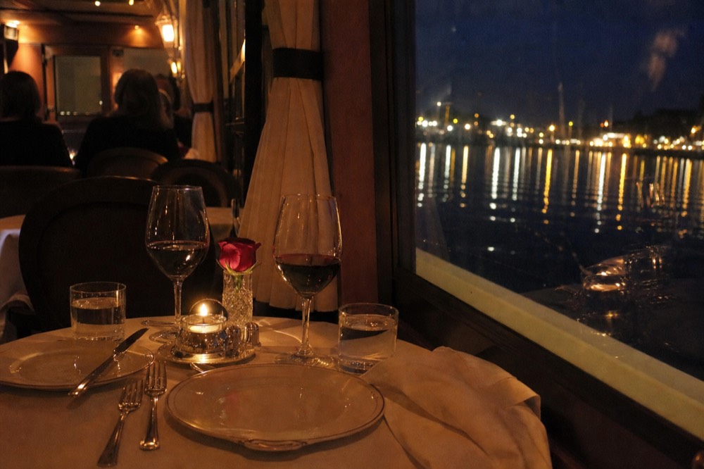 Two place settings with wine glasses at a candlelit private table on a dinner cruise