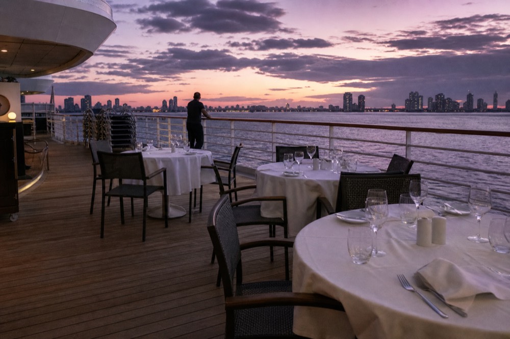 A quiet dinner cruise deck at dusk with a few tables and the city skyline behind