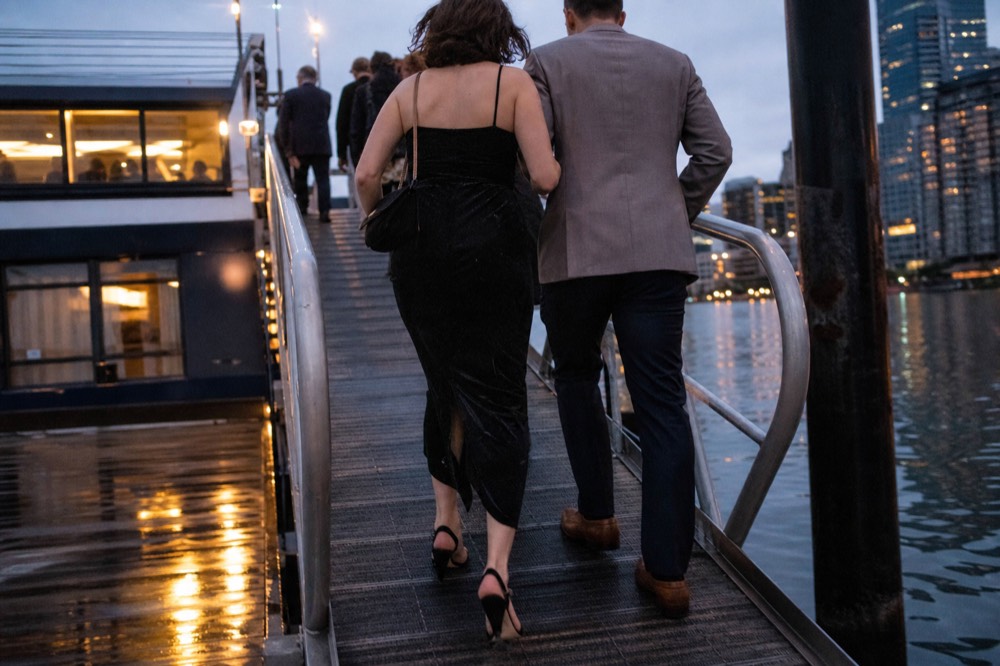 A woman in a cocktail dress and a man in a jacket walking a cruise ship gangway in the evening